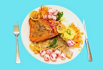 Fried trout with rice and vegetable strips on white plate, isolated on blue background