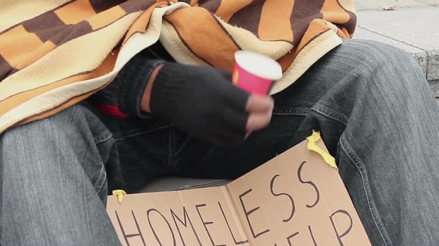 Poor man begging, shaking cup to draw attention, people giving money to homeless