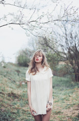 young beautiful blonde girl posing in white shirt on the street next to a lilac tree, flowers, spring, tender portrait, red lips, a warm mood outdoor fashion portrait, close up