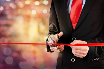 Businessman cutting red ribbon with pair of scissors close up
