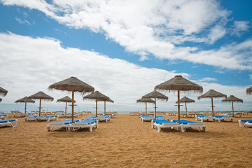 Fototapeta premium Lounge chairs with umrellas on the empty sandy beach in Albufeira, Portugal. Idyllic travel background.