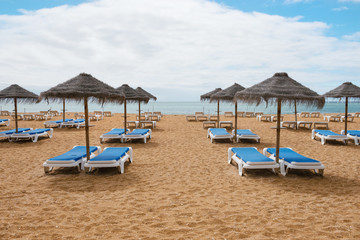 Lounge chairs with umrellas on the empty sandy beach in Albufeira, Portugal. Idyllic travel background.