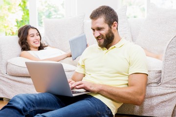 Couple using laptop and digital tablet in living room