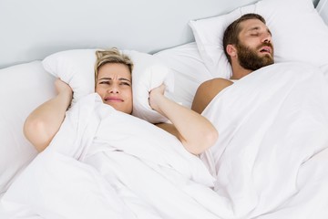 Fototapeta na wymiar Woman covering ears while man snoring on bed