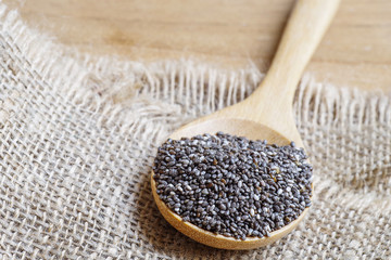Chia seeds, super food, in wooden spoon on burlap and wood backg