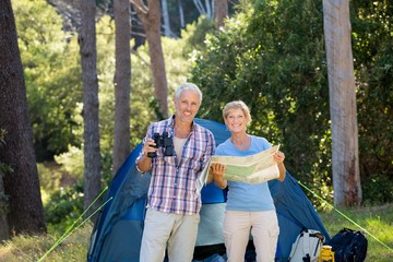 Mature couple smiling and holding binoculars and map