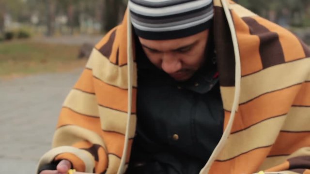 Frozen man covered with blanket asking for alms in the street, homelessness