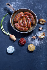 Baked sausages in a frying pan, three meat sauce, and grilled onion on a dark background. Place for inscription.