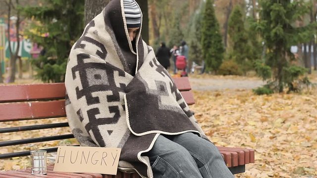 Hungry homeless frozen man sitting on bench and trying to get warm, poverty