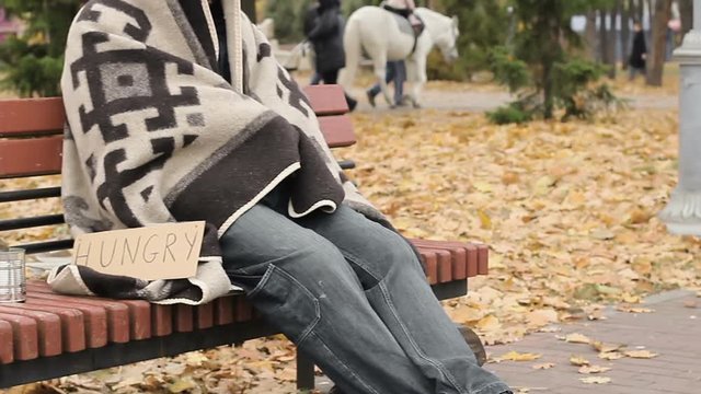 Poor homeless person sitting on bench with hungry sign, begging for spare change