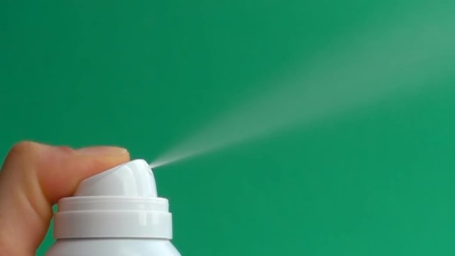 close up spraying aerosol deodorant in slow motion over green background