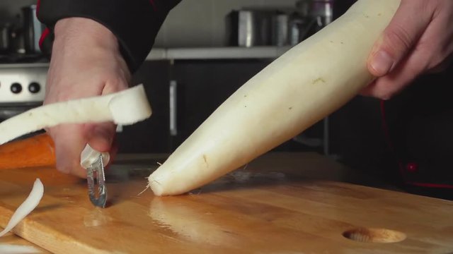 SLOW: A cook cleans a daikon on a cutting board in a restaurant kitchen