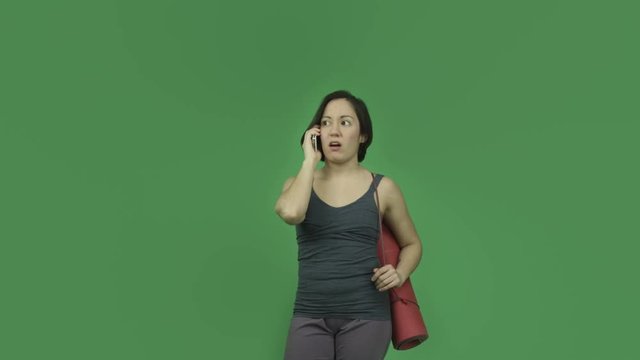 caucasian sporty girl with yoga mat isolated on green screen talking with cell phone