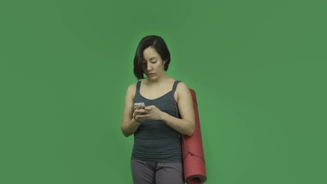 caucasian sporty girl with yoga mat isolated on green screen using cell phone