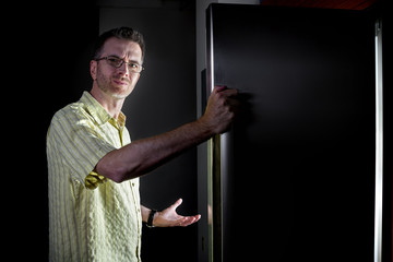 Man looking for food in an open fridge in a dark kitchen late at night