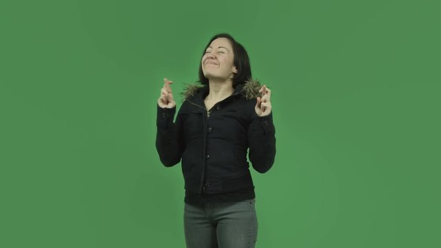 caucasian girl with winter jacket isolated on green screen with fingers crossed