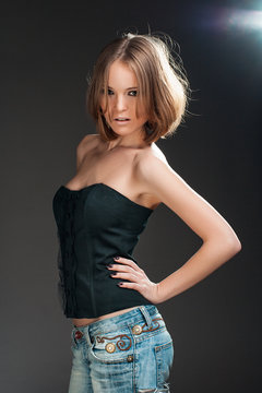 Sexy beautiful young woman posing on bark background, looking at camera. Girl in jeans and black fashionable top.