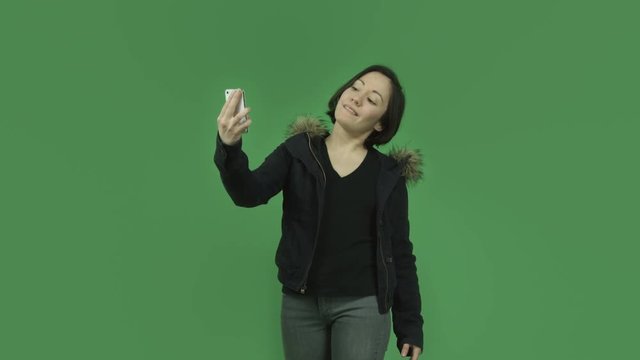 caucasian girl with winter jacket isolated on green screen taking selfie