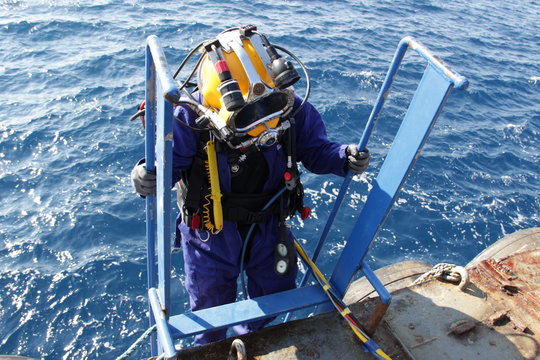 Photo of a diver in suit and helmet, which descends from the ship down to the water