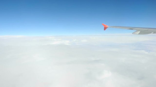 Flight of the airplane in the environment of the cumulus clouds. Fluffy white clouds view from above, in the sky. The wing of the plane cuts the atmosphere in the air.