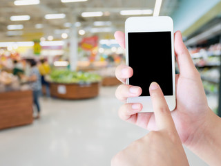 Female hand holding mobile phone on grocery store blur backgroun