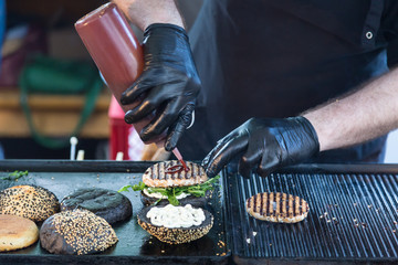 Chef making beef burgers outdoor on open kitchen international food festival event. Street food ready to serve on a food stall.