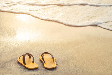 Fototapeta na wymiar Yellow flip flop on the beach with bright light of sunset in summer