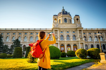 Young female tourist photographing with smart phone museum of Art History in Vienna.
