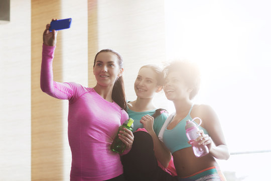 happy women with smartphone taking selfie in gym