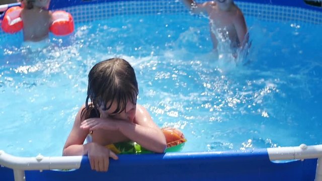 Playful, naughty boy splashes water into the small girls in the pool
