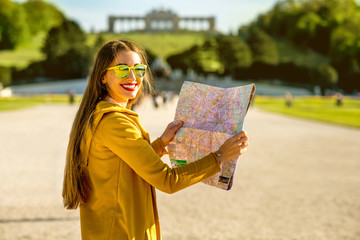 Young female tourist traveling with paper map in Schoenbrunn palace with Gloriette building on the background