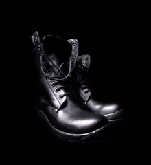 a pair of black leather military boots on black background