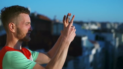 young man taking picture of a city from a balcony using smartphone slow motion
