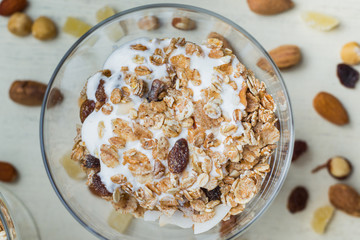 Granola with yoghurt, nuts and fruits in glass bowl on light background. Delicious, healthy sweet dessert for breakfast. Cereal, muesli.  Copy space, closeup.
