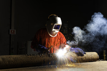 The worker welding metal in manufacturing plant, sparks flying o
