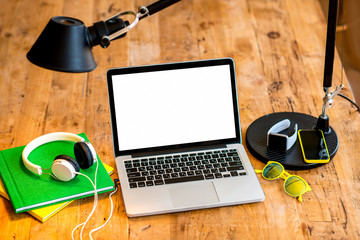 Laptop with white screen with earphones, smart watch, books, smart phone glasses and lamp on the...