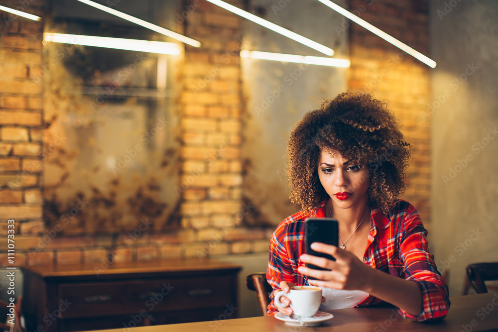 Wall mural young woman at cafe drinking coffee and using mobile phone