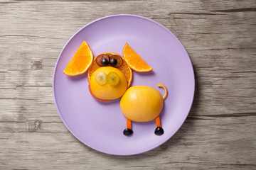 Funny pig made of orange and grape on plate and wood