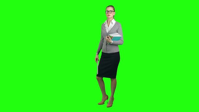 Serious young woman teacher standing on green screen background, holding books and ruler and looking at camera