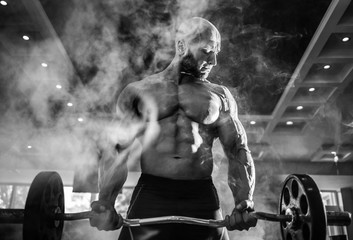 Young handsome caucasian bodybuilder sportsman working out with a barbell in gym, doing biceps...