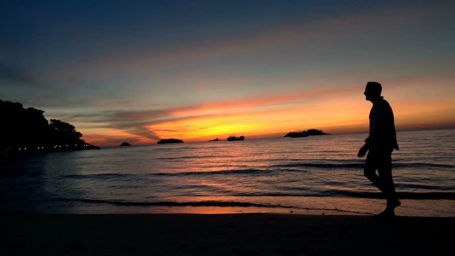 Silhouette of man walking on beach during sunset, super slow motion 120fps
