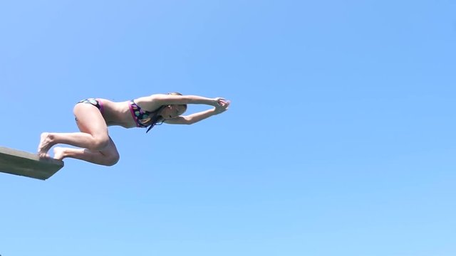 Playful teenage girl takes header jump from the springboard into sea water.
