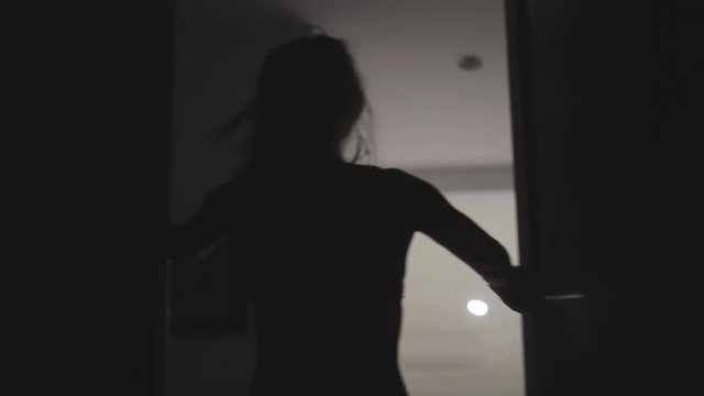 Silhouette of young thin attactive woman in underwear dancing in the doorway in the dark. Shadows and reflections. Woman standing in the doorway.Handheld shot.