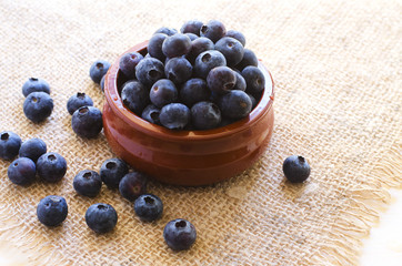 Fresh blueberries in clay bowl on sacking  background 