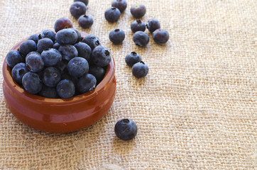 Fresh blueberries in clay bowl on sacking  background with copyspace