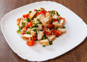 chicken and rice salad with fresh tomatoes in a plate on wooden table