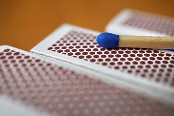 
Safety match stick with a small blue head on the top of box of safety matches with its black striking surface with the honeycomb shapes on the narrower side 