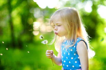 Pretty little blonde girl blowing off a dandelion