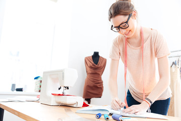 Happy woman seamstress wearing glasses standing and drawing in workshop