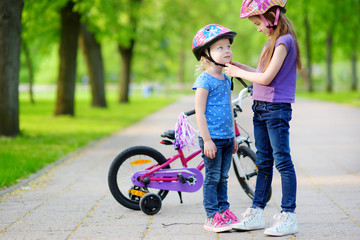 Adorable girl helping her sister to put a bicycle helmet on